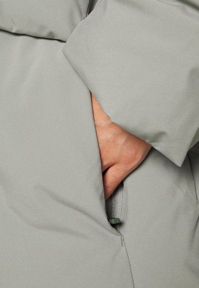 Lyst grå, mat-finish overtøj med en sidelomme; struktureret stof; en hånd synlig inde i lommen, der afslører et glat for.