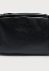 Ορθογώνια τσάντα από μαύρο ψεύτικο δέρμα με λεία υφή και ανάγλυφο λογότυπο της μάρκας. Διαθέτει κλείσιμο με φερμουάρ κατά μήκος της πάνω άκρης.