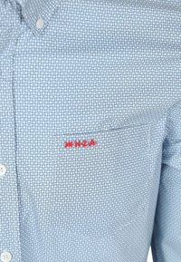 Blauwe shirt met een geometrisch patroon, voorzien van een rode borduursel van "#NZA" op de pocket, gemaakt van katoen, met knopen en een klassieke kraag.