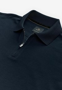 Navy polo skjorta med dragkedja i kragen, texturerad tyg och fårskinnsmönster på kragen. Etiketten säger "NEXT REGULAR FIT."