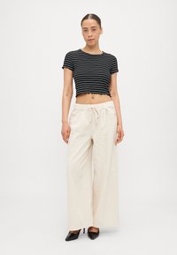 Black and white striped cropped top with scalloped hem paired with beige wide-leg pants and black pointed-toe heels.