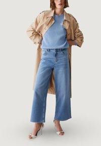 Beež kergtopp mantli kohal helesinise soonikkoega kudum, kombineeritud kõrge vöökohaga laia säärega teksapükstega ja valgete kontsakingadega.