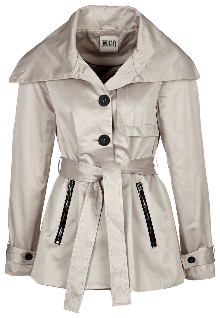 Trench beige con un amplio collar, botones negros, cintura ceñida con cinturón y bolsillos con cremallera. Textura suave y silueta ajustada.