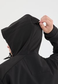 Sort hættejakke med en glat overflade, justerbar snor, og synlige stikninger på hætten og skuldrene.