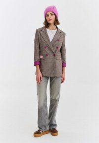 Hnedé kárované dvojradové sako s fialovými akcentmi, kombinované s svetlosivými rozšírenými džínsami a hnedými platformovými topánkami. Nosená ružová čiapka.