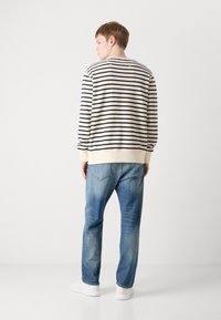 Stripet genser med kremfargede og marineblå horisontale striper, ribbede mansjetter og nederkant, kombinert med lyseblå jeans og hvite joggesko.