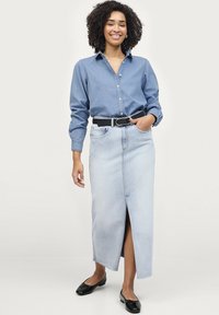 Lyseblå denimnederdel med en frontslids, parret med en mørk denimskjorte med knapper, accentueret af et sort bælte og sorte flade sko.