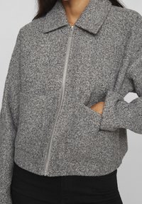 Szara kurtka polarowa z kołnierzem, zamkiem błyskawicznym z przodu i bocznymi kieszeniami. Wykonana z miękkiego, teksturowanego materiału o krótkim kroju.