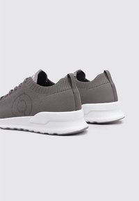 Zapatillas deportivas grises con parte superior de malla texturizada, suela de goma blanca y talón reforzado. Presentan un branding mínimo y un diseño de punta redondeada.