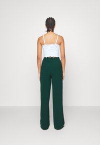 Lace crop top in lichtblauw, met dunne bandjes; gecombineerd met groene wijde broek met elastische tailleband en zachte textuur.