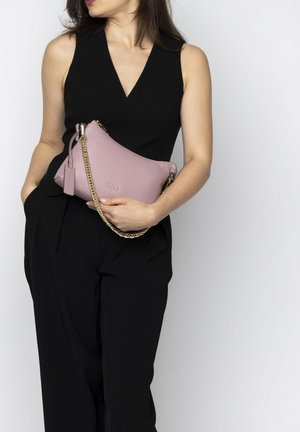 Pink leather bag with a textured finish, gold chain strap, and a small leather tag. Worn underarm with a black outfit.