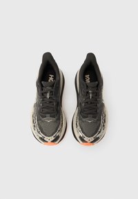 Μαύρα και γκρι παπούτσια τρεξίματος με υφασμάτινη επάνω επιφάνεια, λεπτομέρειες από δίχτυ και φωτεινή πορτοκαλί σόλα. Κορδόνια και λογότυπα δίνουν έμφαση στο σχέδιο.