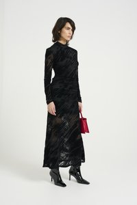 Černé dlouhé rukávy šaty s texturovaným vzorem, přiléhavým tělem a splývavou sukní. V kombinaci s lesklými černými kotníkovými botami a malou červenou kabelkou.
