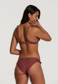 Bordeaux bikini set met verstelbare bandjes, voorzien van een gouden sluiting aan de achterkant en ruches aan de zijkanten van de onderkant. Vloeiende textuur.