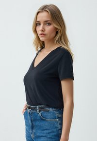 Maglietta nera a V in cotone morbido, con maniche corte e vestibilità slim, abbinata a pantaloni corti in denim blu con vita alta e una cintura nera.