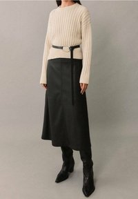 Beige geribbelde trui met lange mouwen, gecombineerd met een zwarte leren midi-rok met een zijnaad en een dunne zwarte riem met een metalen gesp.