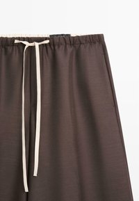 Hnědé lehké kalhoty s elastickým pasem a bílým šňůrkou. Hladká textura s jednoduchým designem, bez vzorů nebo zdobení.