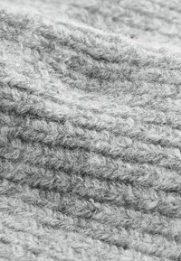 Grau gestrickter Stoff mit einer weichen, strukturierten Oberfläche, die ein lockeres Gewebe und sichtbare Fasern aufweist, wodurch ein einladendes, warmes Aussehen entsteht.