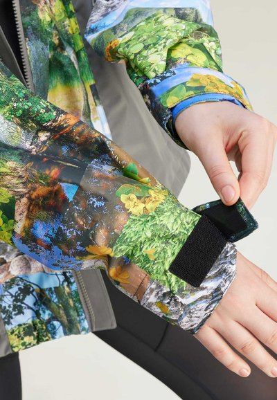 Chaqueta de manga larga con un estampado de naturaleza multicolor, que presenta paneles verdes, amarillos y azules. Incluye un cierre de puño de Velcro negro.