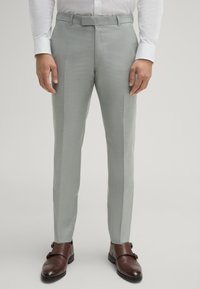 Hellgraue, maßgeschneiderte Hose aus strukturiertem Stoff, schlanker Schnitt und glatter Bund. Braune Leder Schuhe ergänzen das Outfit.