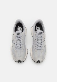 Lys grå sneakers med en blanding av semsket skinn og mesh-materialer, strømlinjeformet design, flate snører og en tykk svart og hvit såle.