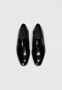 Svarta lackläderloafers med en elegant, spetsig form. Har ett framträdande band över vristen. Diskret logotyp på sidan.