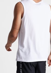 Camisa sin mangas blanca con un escote redondo y un ajuste relajado. Fabricada en algodón suave, presenta costuras mínimas y sin logotipos visibles.