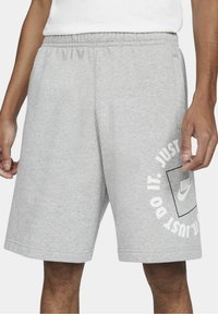 Pantalones cortos de algodón gris con una cinturilla elástica. Presenta un logo de Nike impreso y "Just Do It" en texto blanco en la pierna izquierda.
