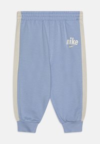 Svijetloplave trenirke s bež bočnim panelima, elastičnom strukom i rebrastim manžetama. Ima bijeli Nike logo na lijevoj nozi.