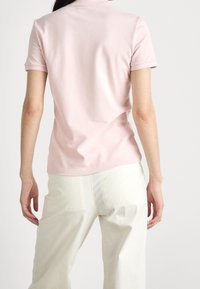 Kortärmad polotröja i mjuk rosa, med en klassisk krage och slät textur, kombinerad med ljusa, löst sittande byxor.