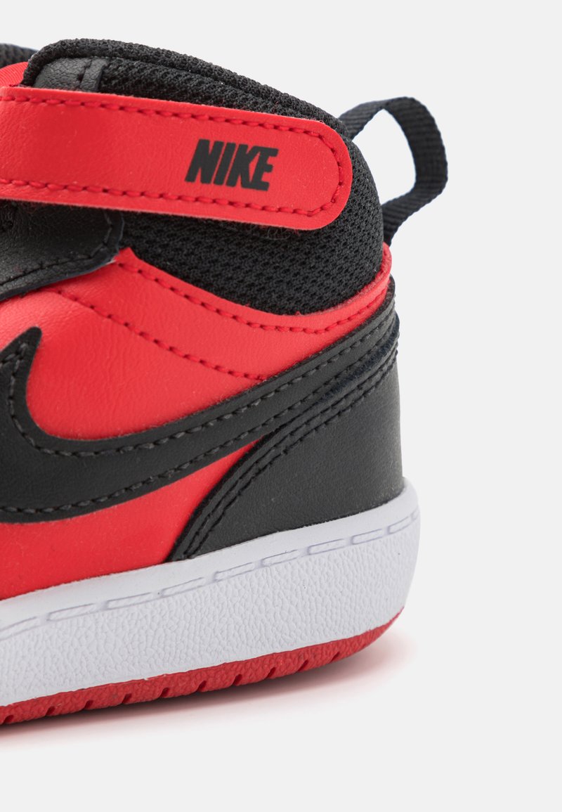 Zapatilla Nike en cuero negro y rojo, con parte superior de malla, cuello acolchado, suela blanca y correa de Velcro con detalle del logo.