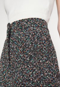 Textured black skirt with multicolored flecks in green, orange, and white. Features a high waist and a side zipper closure.