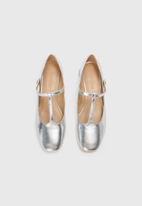 Silver ballet flats with a T-strap design, rounded toes, and a smooth leather texture. Interior is a light tan leather.