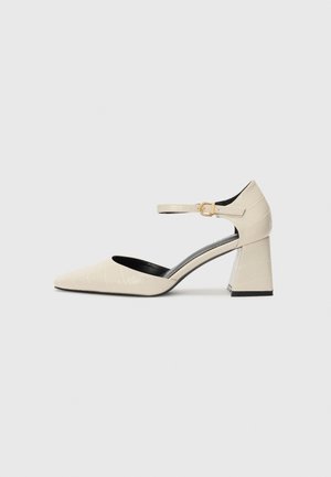 Beige faux leather block-heeled shoes with a pointed toe, ankle strap, and subtle crocodile texture detailing. Black inner lining.
