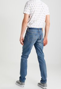 Vaaleansiniset suoralahkeiset farkut ompelukoristein, yhdistetty valkoiseen kuvioituun t-paitaan ja harmaisiin lenkkareihin.