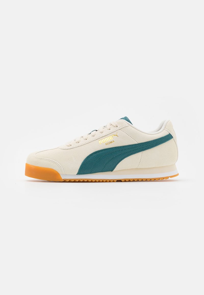 Sneaker in suede beige con dettagli in teal, marchio dorato e suola in gomma arancione. Presenta una punta arrotondata e un design classico con lacci.