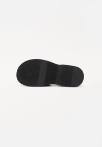 Black rubber shoe sole featuring a textured surface, smooth sections, and a printed logo; flat profile with a rounded shape.