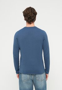 Niebieski dziany sweter z długim rękawem o prążkowanej fakturze i okrągłym dekolcie, zestawiony z jasnoniebieskimi dżinsami. Widok z tyłu ukazuje bezszwowy design.