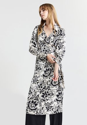 Abito a wrap floreale in bianco e nero, con colletto, maniche lunghe e un design fluido caratterizzato da un pronunciate motivo floreale.