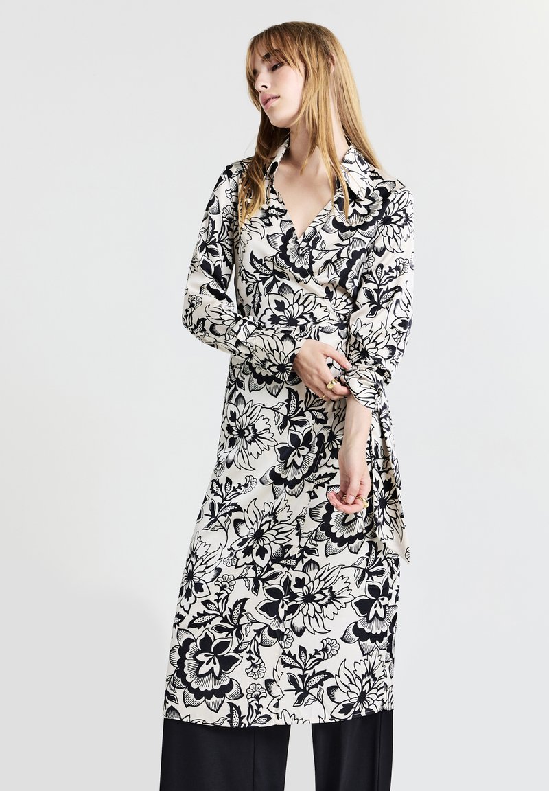 Robe portefeuille fleurie en noir et blanc, dotée d'un col, de longues manches et d'un design fluide avec un motif floral prononcé.