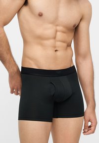 Αντρικός κορμός με μαύρα μπόξερ, που δείχνει καθορισμένους κοιλιακούς και χέρια, σε απλό φωτεινό φόντο.