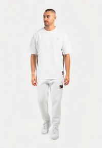 Camiseta blanca de algodón con mangas cortas, cuello redondo y un pequeño logo, combinada con pantalones de chándal blancos a juego con parches de logo.