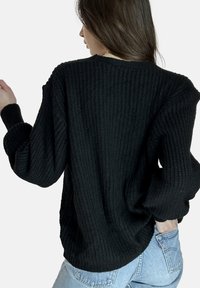 Zwarte gebreide trui met een geribbelde structuur, verlaagde schouders en brede mouwen. Gekozen boven lichtblauwe spijkerbroek met een losse pasvorm.