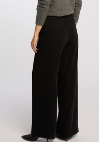Black wide-leg pants made of soft fabric, featuring an elastic waist and a clean, unembellished design. Smooth texture with no visible patterns.
