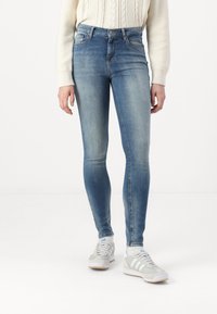Fakó kék skinny farmernadrág sima textúrával, öt zsebes dizájnnal és övhurkokkal, krémszínű pulóverrel és fehér sportcipővel párosítva.