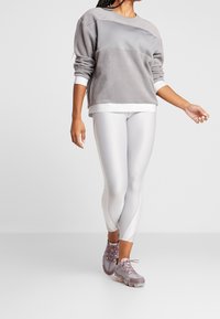 Grå fleece sweatshirt med en blød tekstur, paired med glansfulde hvide leggings. Fodtøj er lyserøde og grå sneakers med en gennemsigtig sål.