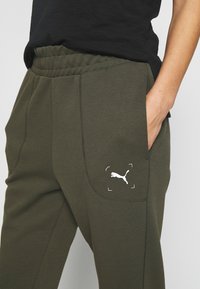 Sportliche Jogginghosen aus dunkelolivgrünem Stoff, mit einem gerippten Bund, Seitentaschen und einem weißen Puma-Logo auf der Vordertasche.