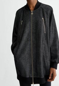 Giacca bomber nera con un effetto metallico testurizzato. Presenta tasche con zip e un colletto a costine. Vestibilità semplice e rilassata con maniche lunghe.