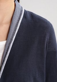 Námořnický pletený cardigan s pruhem bílého a modrého límce, s hladkou textura a jemnými švy podél okrajů.