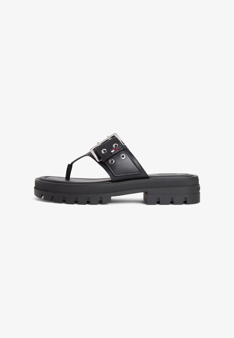 Σανδάλι με μαύρη χοντρή σόλα, φαρδιά λωρίδα, ασημένια αγκράφα και διάφραγμα δακτύλων, με μικρό κόκκινο, λευκό και μπλε λογότυπο στη πλευρά.